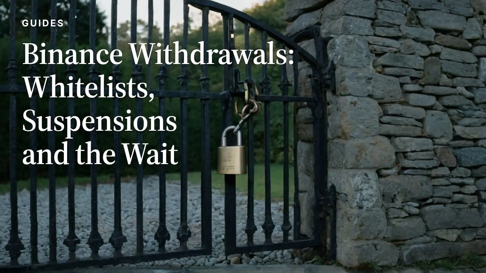 A black wrought-iron gate set into a dry-stone wall, held shut by a brass padlock at dusk.