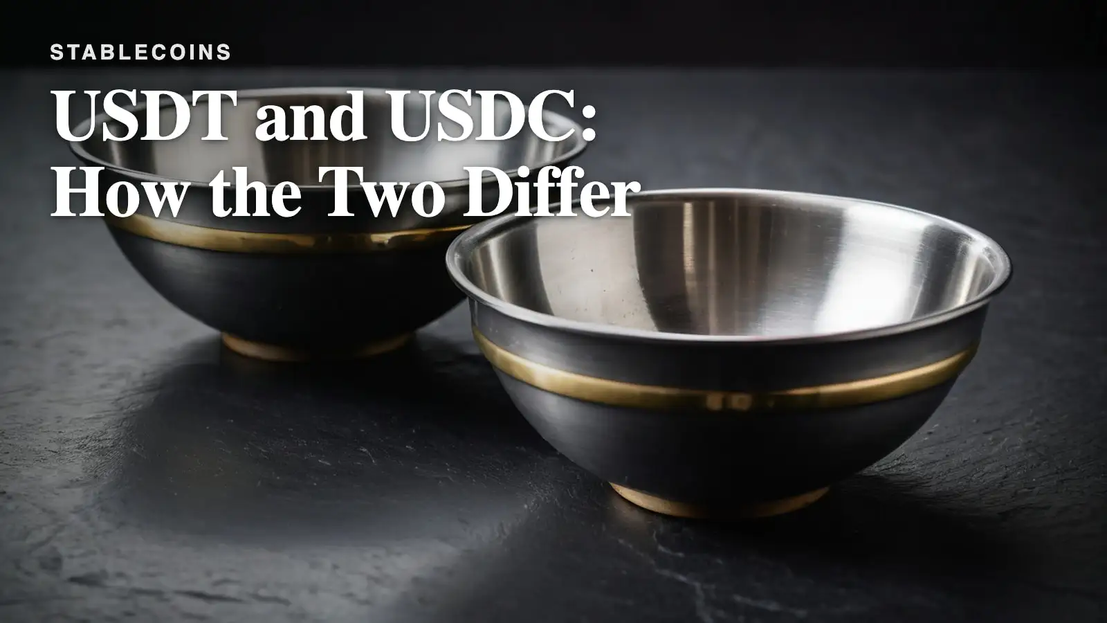 Two brushed steel bowls with a brass band, side by side on a dark slate surface under hard side light.
